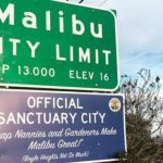 Fake but real-looking Malibu sign posted below a "Malibu City Limit" sign that reads "Official Sanctuary City, Cheap Nannies and Gardeners Make Malibu Great! (Boyle Heights Not So Much)"