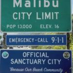 Fake but real-looking Malibu sign posted below a "Malibu City Limit" sign that reads "Official Sanctuary City, Because Our Beach Community Needs Cheap Labor, Dude."