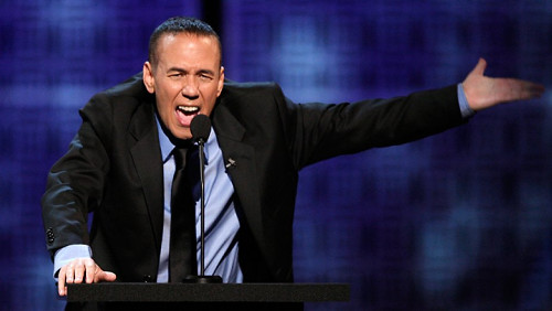 Gilbert Gottfried talking standing behind a podium and talking into a microphone. [Formatted]