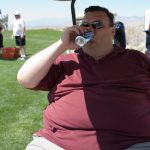 Obese golfer sitting on a golf cart drinking Bud Light.