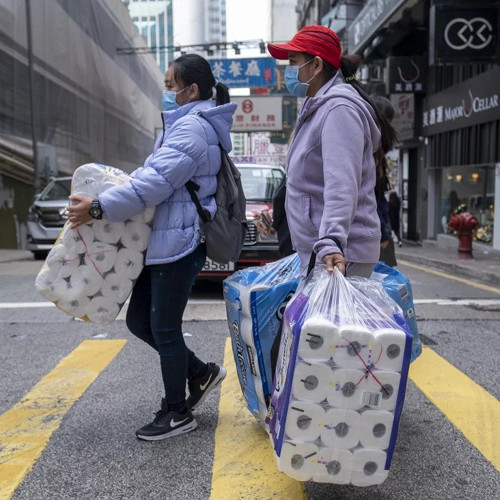 Two women wearing surgical masks and carrying multiple giant bags of toilet paper. [Formatted]